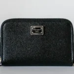 A black wallet resting on a wooden table surface, showcasing its sleek design and texture.